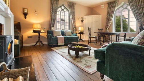 The sitting room at Blickling Tower with two large windows, a woodburner, two sofas and a dining table with two chairs